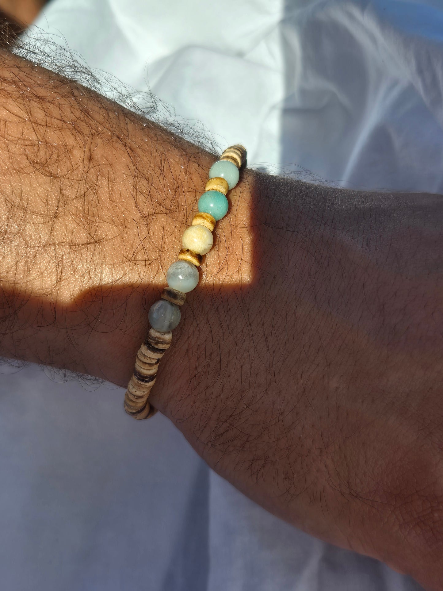 Elastisches Armband aus Kokosnuss- und Quarzperlen, getragen am männlichen Handgelenk, vor einem weissen Stoffhintergrund.
