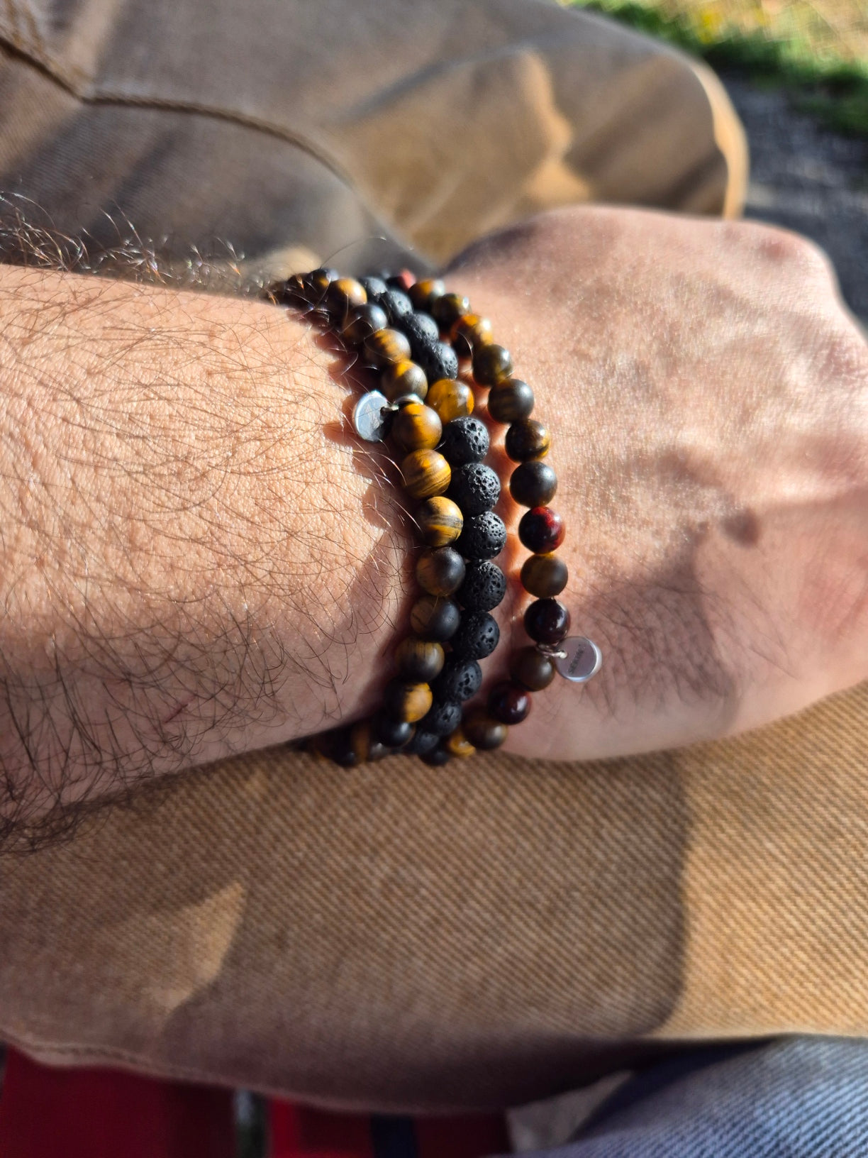 Drei verschiedene Armbänder an einem Herren-Handgelenk. Mit Lavaseinen und Tigerausge-Steinen