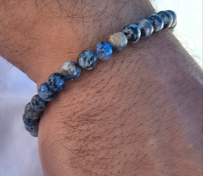 Elastisches Armband aus blau grauen Quarzperlen mit einem silbernen Sekino Anhänger, getragen am männlichen Handgelenk, vor einem weissen Stoffhintergrund