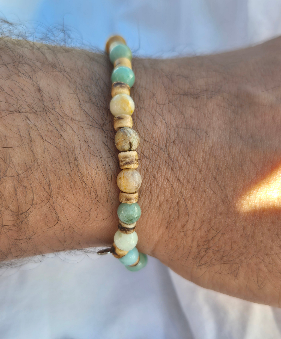 Elastisches Armband aus Quarz- und Kokosnussperlen, getragen am männlichen Handgelenk, vor einem weissen Stoffhintergrund