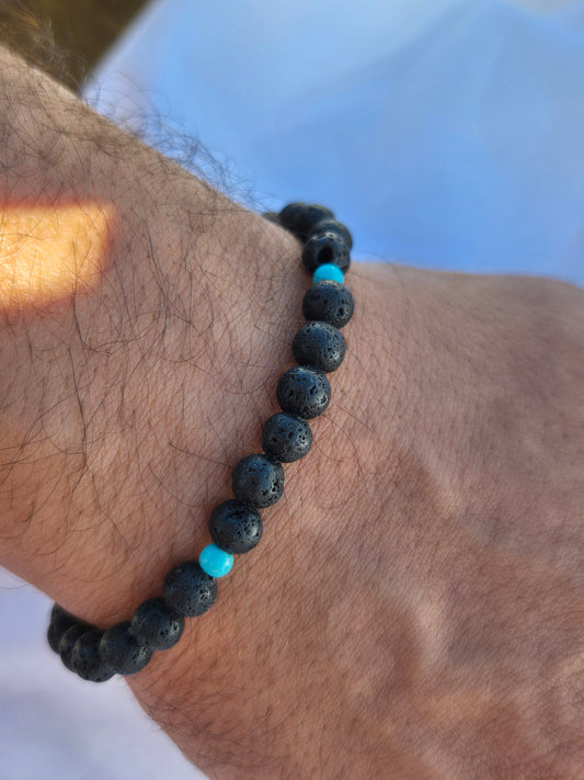 Elastisches Armband aus Lavasteinperlen und türkisen Holzperlen mit einem silbernen Sekino Anhänger, getragen am männlichen Handgelenk, vor einem weissen Stoffhintergrund