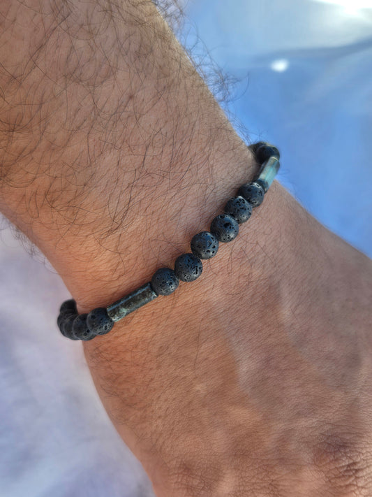 Elastisches Armband aus Lavasteinperlen und Tubeförmigen Eruptivgestein Perlen mit einem silbernen Sekino Anhänger, getragen am männlichen Handgelenk, vor einem weissen Stoffhintergrund