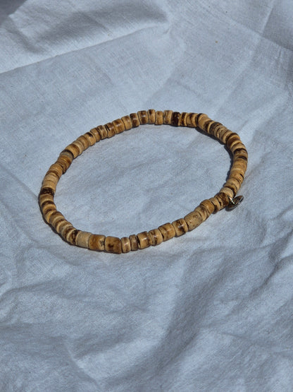 Elastisches Armband aus flachen Kokosnussperlen, auf einem weissen Stoffhintergrund liegend.