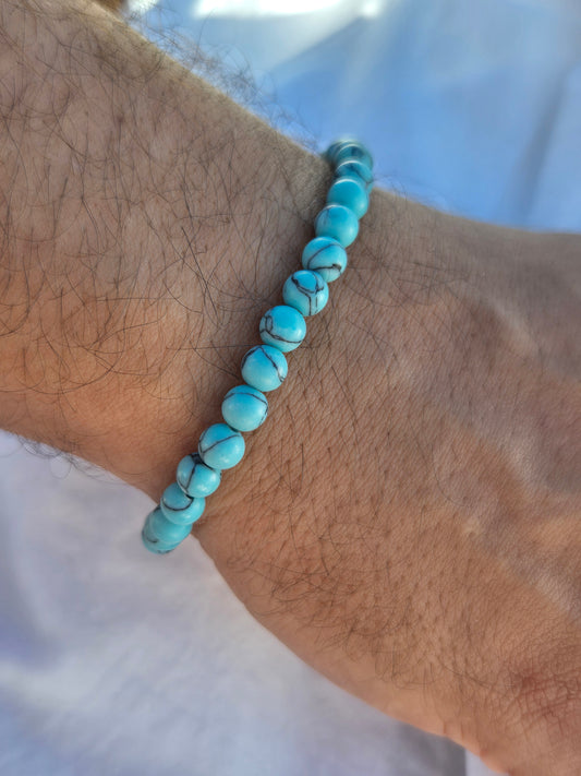 Elastisches Armband aus türkisen Calcitperlen im Marmorlook mit einem silbernen Sekino Anhänger, getragen am männlichen Handgelenk, vor einem weissen Stoffhintergrund