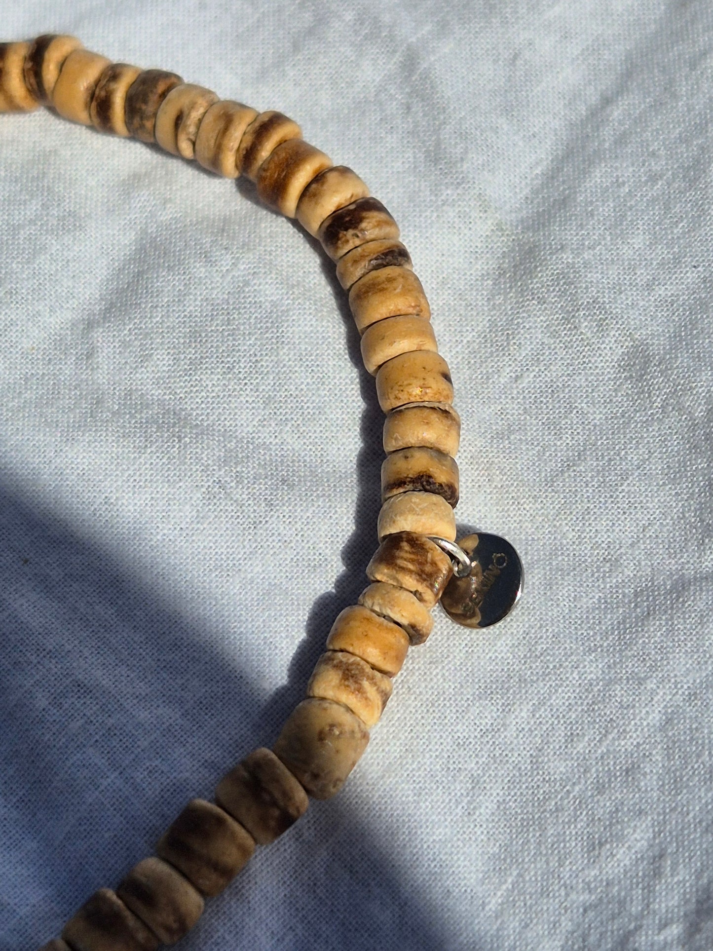 Ausschnitt von elastischem Armband aus flachen Kokosnussperlen, auf einem weissen Stoffhintergrund liegend.