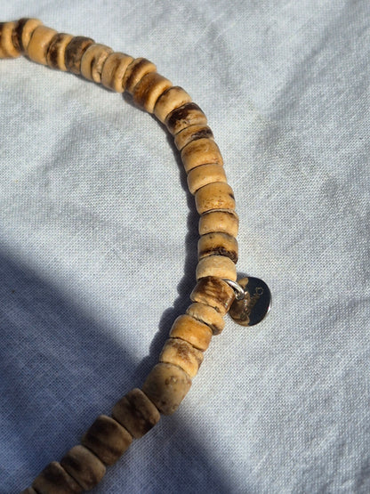 Ausschnitt von elastischem Armband aus flachen Kokosnussperlen, auf einem weissen Stoffhintergrund liegend.