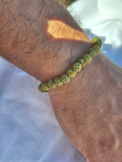 Elastisches Armband aus grünen Lavasteinperlen mit einem silbernen Sekino Anhänger, getragen am männlichen Handgelenk, vor einem weissen Stoffhintergrund