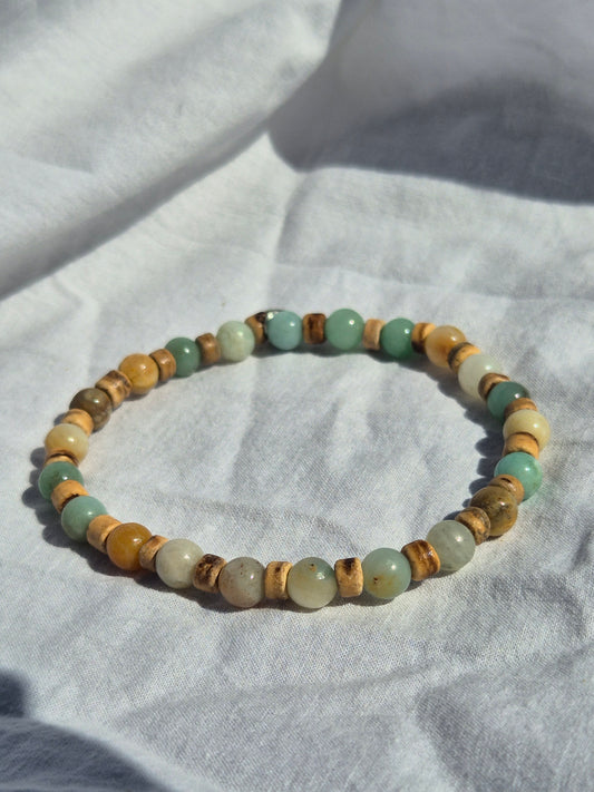 Elastisches Armband aus abwechselnd runden Quarzperlen in Türkis-, Gelb- und Beigetönen sowie flachen Kokosnussperlen, auf einem weissen Stoffhintergrund liegend.